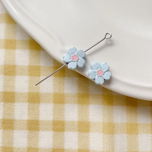 Detail of light blue enamel flower charms with eye pin on a white ceramic plate