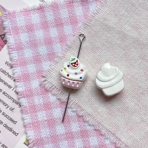Détail d'un charme cupcake DIY avec motif fraise et aiguille sur tissu à carreaux