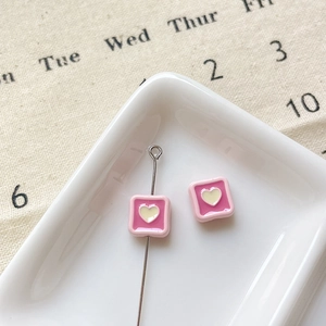Gros plan de pendentifs carrés en émail rose avec motif cœur pour la création de bijoux