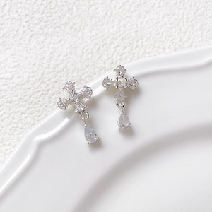 Close-up of asymmetric silver cross earrings with zircon pavé and teardrop charms