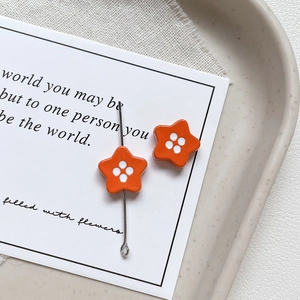 Macro shot of orange star-shaped charm with white dots on a silver needle for DIY jewelry