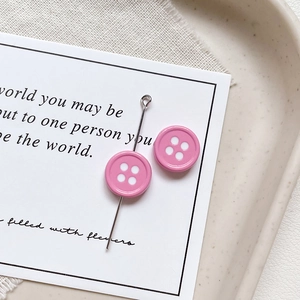 Detailed view of pink button-shaped charm with white dots on an elegant beige tray