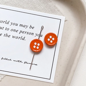 Close-up of bright orange button-shaped stud earrings with four-hole design on tray
