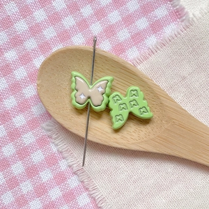Macro detail of two butterfly-shaped resin DIY sewing notions with a metal pin and star pattern