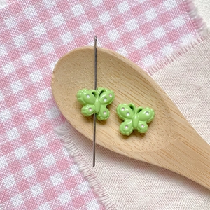 Close-up of green butterfly beads with white dots being threaded for DIY jewelry