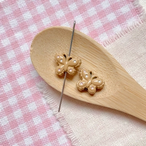 Detail of brown butterfly bead with pink dots in wooden spoon for DIY jewelry making