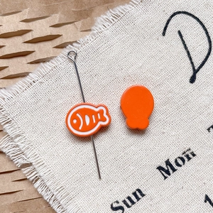 Détail de breloques poissons en émail orange avec rayures pour création de bijoux DIY