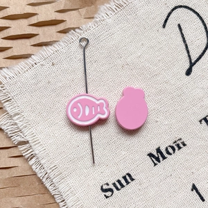 Gros plan de charms de poisson rose en émail pour bijoux DIY sur lin et papier alvéolé