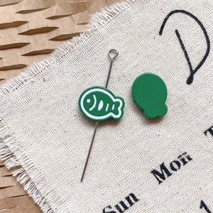 Gros plan de breloques poisson vertes pour bijoux DIY sur fond de lin et papier kraft brun