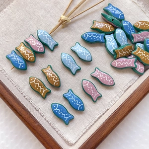 Detail of colorful striped fish-shaped beads for handmade DIY jewelry making on white fabric
