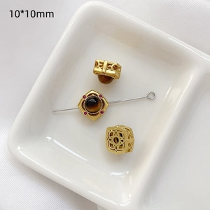 Detalle de cuentas doradas con piedra ojo de tigre y circón rojo de 10x10mm