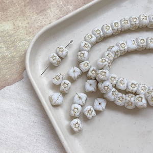 Macro detail of white cubic Czech glass beads with golden sun pattern and vintage finish