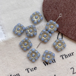Close-up of square blue Czech glass beads with gold sunflower pattern for DIY jewelry