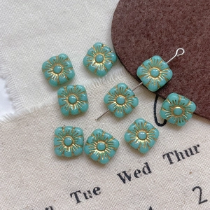 Macro view of square Czech glass beads with vintage golden floral patterns for DIY jewelry