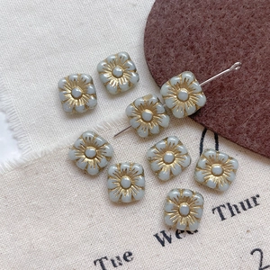 Macro view of square blue glass beads with gold floral details for DIY jewelry making