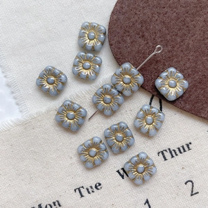 Detailed view of light blue square glass beads with golden floral engraving for DIY jewelry