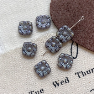 Macro view of six square floral glass beads with embossed petals and metallic luster