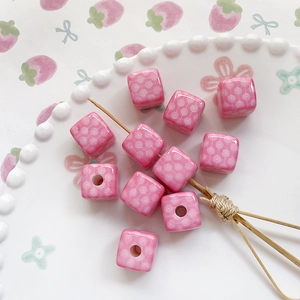 Pink cube beads with white spiral patterns for DIY jewelry making on white ceramic plate
