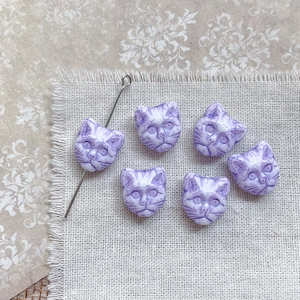 Detailed view of six marbled purple cat head beads on a rustic linen background