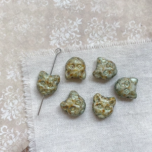 Macro detail of cat head ceramic beads in celadon glaze with metallic display needle