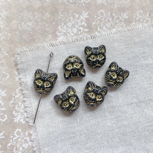 Macro shot of 6pcs black and gold vintage cat-head glass beads on linen fabric