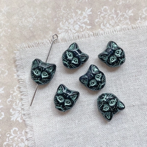 Detailed view of vintage black cat head beads with green patina for jewelry making
