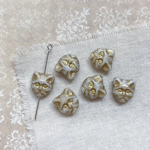 Close-up of white cat-shaped beads with gold details for DIY jewelry on linen cloth