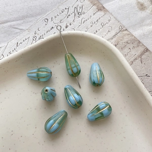 Macro detail of blue and green Czech glass teardrop beads with golden striped edges
