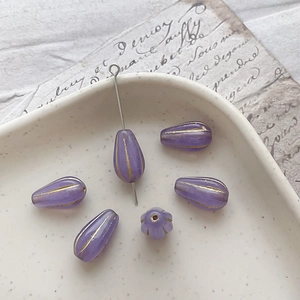 Macro detail of violet glass teardrop beads with gold stroke for DIY jewelry making