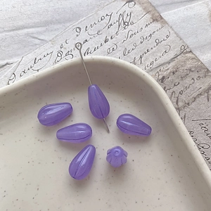 Close-up of translucent purple teardrop glass beads with vertical striped texture for DIY crafts