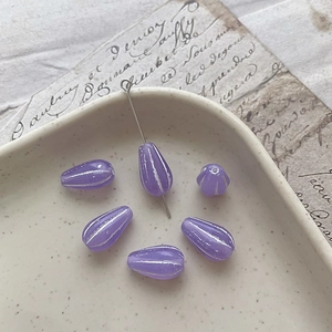 Macro shot of matte lavender Czech glass teardrop beads with white stripes in a ceramic dish