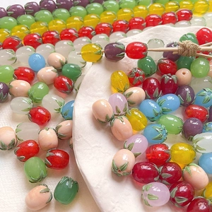 Macro shot of colorful glass strawberry beads for DIY jewelry making on white ceramic