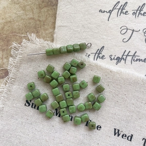 Macro shot of green Picasso glass cube beads with vintage brown edges on rustic burlap