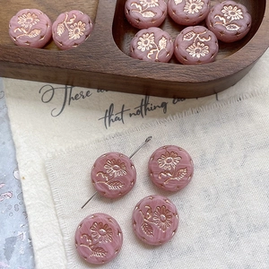 Detailed macro view of pink glass beads with floral relief and golden edges on wood