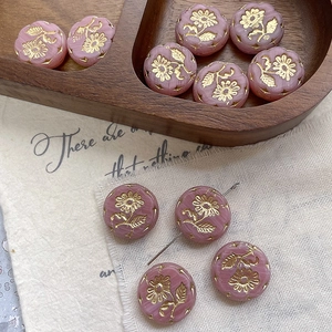 Detailed view of pale pink glass floral beads with gold embossed flower on wooden tray