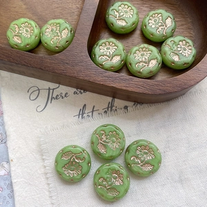 Macro view of vintage green daisy beads with gold flower engraving on a wooden tray