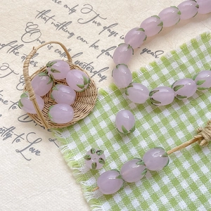 Macro detail of tulip glass beads for DIY jewelry with soft pink petals and green leaves