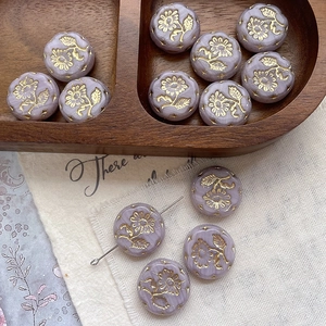 Macro view of vintage lavender glass flower beads with golden embossed daisy patterns