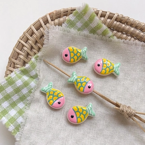 Close-up of five colorful hand-painted fish resin beads on a white linen cloth background