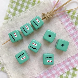 Close-up of mint green square resin beads with hand-painted quirky facial expressions