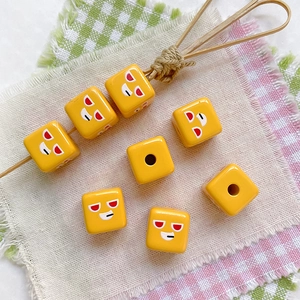 Macro view of yellow cube beads with cartoon expressions for DIY phone chains and jewelry