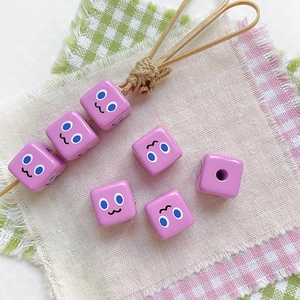 Macro detail of pink square DIY beads with cartoon facial expressions and pre-drilled holes