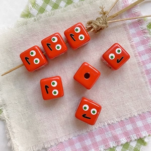 Macro detail of red cube beads with cartoon expressions for DIY handmade jewelry crafts