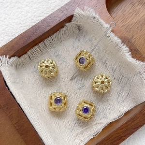 Detalle de cuentas huecas bañadas en oro de 18k con circonitas púrpuras en lino