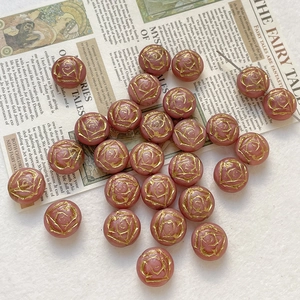 Macro detail of dusty rose glass beads with gold painted rose patterns for DIY jewelry