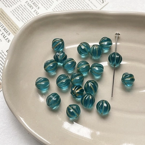 Macro shot of lake blue pumpkin beads with gold accents on a ceramic craft tray