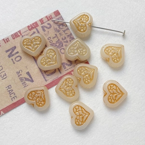 Macro shot of heart-shaped beige glass beads with vintage gold patterns for DIY jewelry