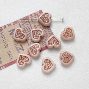 Macro detail of nude pink heart-shaped glass beads with bronze floral relief for DIY jewelry