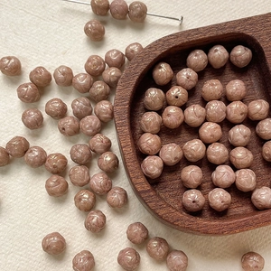 Close-up of 8mm dusty rose Czech glass beads with intricate engraved floral patterns