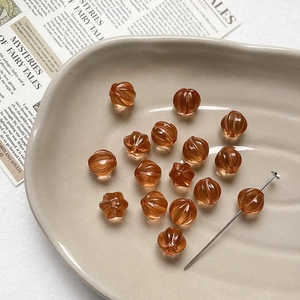 Macro shot of amber pumpkin glass beads and flower charms in a ceramic tray
